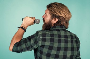 Melodiyi yakala. Olgun karizmatik erkek vokalist. Mikrofonda şarkı söyleyen sakallı adam. Sahnede özgüven ve karizma. Kareli gömlek giyen sakallı bir adam. Rock müzik. Erkek karaoke şarkıcısı