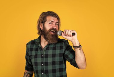 Seve seve söylerim. Erkek karaoke şarkıcısı. Olgun karizmatik erkek vokalist. Mikrofonda şarkı söyleyen sakallı adam. Sahnede özgüven ve karizma. Kareli gömlek giyen sakallı bir adam. rock müzik