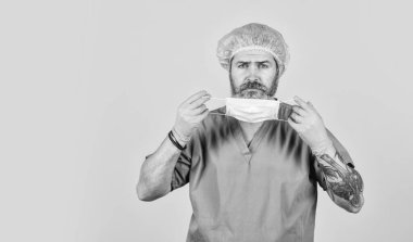 Maske takıyordu. Koruyucu işlevler. İnsanları virüsten korumak. Virüs salgınının başlangıcı. Sakallı doktor üniforması, sarı arka plan. Bir çeşit virüs. Coronavirus konsepti. Virüs mutasyona uğrayabilir.