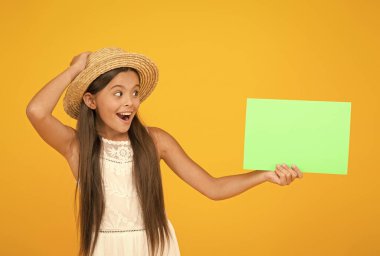 Yeni haberleri paylaşıyoruz. Çocuklar için plaj modası. Sarı arka planda küçük bir çocuk. Yaz kampı aktivitesi. kopyalama alanı. Yaz tatili ve tatil. Mutlu çocukluk. Şaşırmış küçük kız kağıt çarşaf tutuyor.