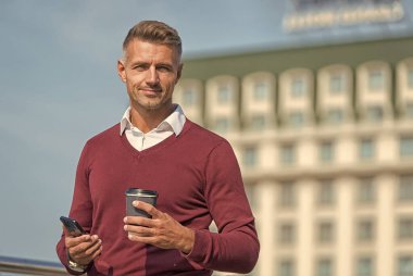 Yemek molası. Kahve molası ve hoş bir sohbet. Cep telefonu. İnternet sörfü. Rahatlatıcı. Açık havada akıllı telefonu ve kahve fincanı olan bir adam. Kahve iç ve rahatla. Günlük ritüeller. Aileyi arama zamanı.