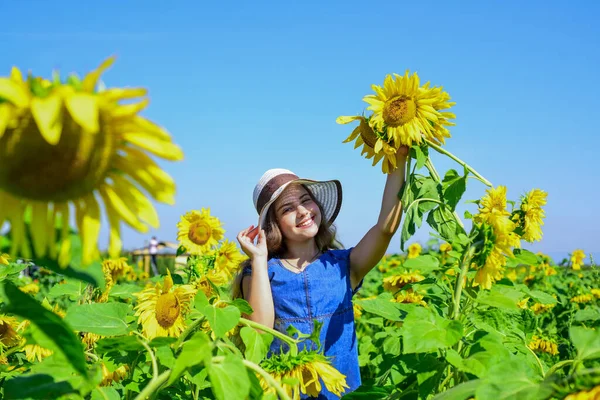 Χαρούμενη παιδική ηλικία. όμορφο κορίτσι φορούν ψάθινο καλοκαιρινό καπέλο στον τομέα. Όμορφο παιδί με λουλούδι. ομορφιά της καλοκαιρινής φύσης. Κοριτσάκι σε χωράφι με ηλιοτρόπια. κίτρινο λουλούδι ηλιοτρόπιου. Κήπος κρεβάτι — Φωτογραφία Αρχείου