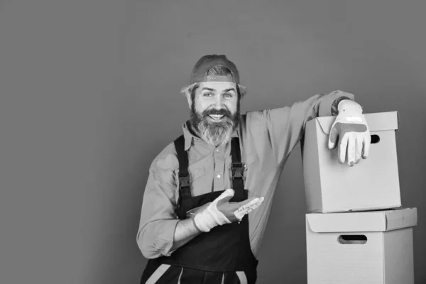 Verhuizen naar een nieuw appartement. Post dienst. Baard lader in uniform. Renovatievoorbereiding. Binnenshuis bebaarde hipster. Nieuw huis. Uitpakken van verhuisdozen. Verhuisdag. Baard man koerier houden dozen — Stockfoto