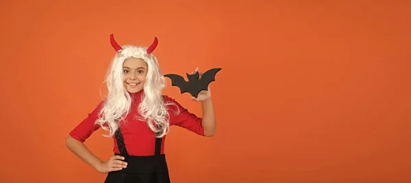 Happy kid on Halloween wear funny carnival costume and horns indoor holding small bat, trick or treat. copy space — Stock Photo, Image