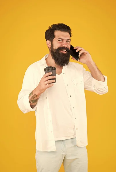 Cara alegre com bigode e barba beber café e falar no smartphone. homem barbudo maduro falar ao telefone enquanto bebe café da manhã. bebida quente em copo de papel. vida moderna — Fotografia de Stock
