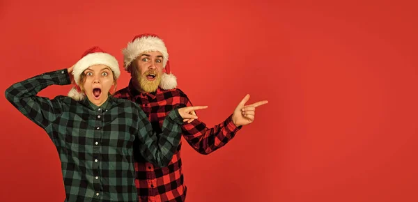 Idea para divertirse. Buen humor. Alegría invernal. Pareja en el amor apuntando espacio de copia. ¡Mira esto! Al estilo de Papá Noel. En Navidad. Hombre y mujer celebración navideña. Compras familiares. Fiesta de Navidad — Foto de Stock