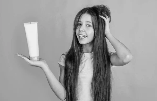 Menina criança alegre com longo cabelo liso segurar condicionador xampu ou garrafa de gel, cuidado do cabelo — Fotografia de Stock