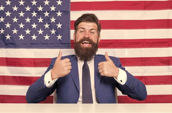 Uczynić naszą ziemię absolutnie najlepszym krajem. Szczęśliwy hipster podnosi kciuki. Kontekst flagi USA. Brodaty mężczyzna gestykulujący kciuki w górę. Gest aprobaty. Kciuki do góry. Znaki dłoni. Podnieśmy kciuki. — Zdjęcie stockowe