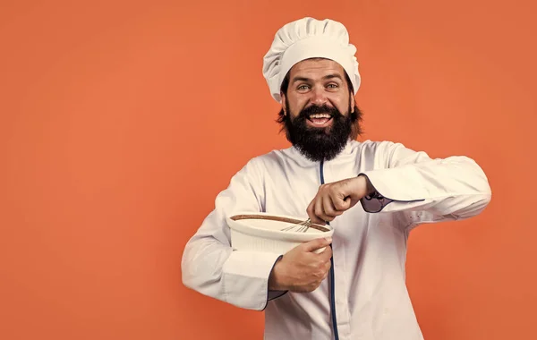 Vrolijke mannelijke chef-kok in hoed met baard en snor op oranje achtergrond kloppen maaltijd met klopper, keuken, kopieer ruimte — Stockfoto