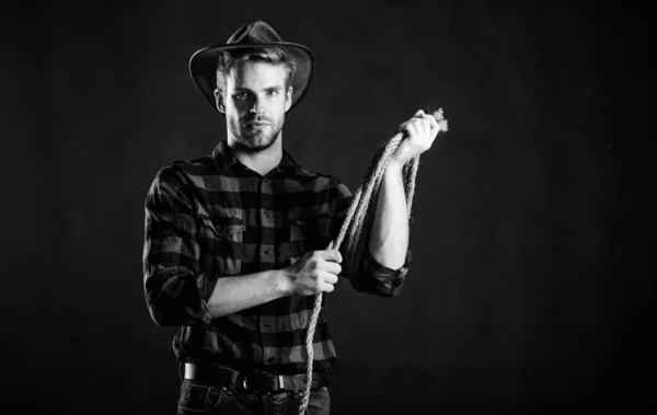 La vida occidental. Hombre sin afeitar fondo negro vaquero. El hombre con sombrero sostiene la cuerda. Herramienta Lasso del vaquero americano. Lasso utilizó cercos competitivos. Lasso puede ser atado o envuelto. Brutal y confiado —  Fotos de Stock