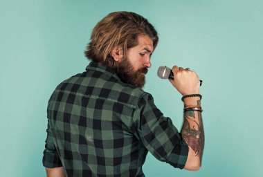 Sadece muhteşem saçlar. Vahşi ve taş gibi. Sakallı adam damalı gömlek giyer ve şarkı söyler. Mikrofonlu erkek şarkıcı. Karaoke konsepti. Erkek şarkıcı müziği sever. Vahşi adam mikrofonla şarkı söylüyor. vokal okulu