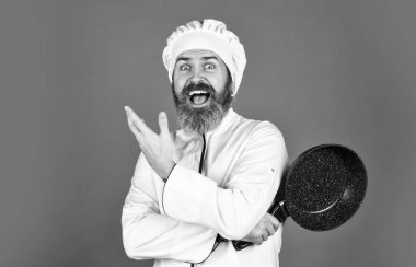 Sakallı aşçı üniforması giyen adam tavayı tutuyor. Profesyonel gibi yemek pişirmek. Evde hazırlanmış ucuz ve lezzetli yemekler. Çok dikkatli ol. Mutfakta yemek hazırlıyorum. Yemek pişirme konsepti. Yüksek kaliteli kızartma tavası