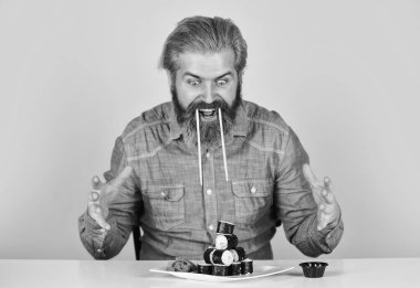 Japon yemek teslimatı. Suşi ruloları. Asya yemeği. Suşi siparişi. Adam evde suşi yiyor. Çubuklu suşi ve zencefil. Japon mutfağı. Doğu kültürü. Sakallı hippi börek yiyor.