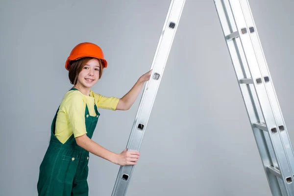 Девушка-работница в защитном шлеме и форме на лестнице, здание — стоковое фото