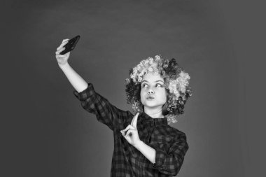 Gökkuşağı peruğu saçlı çocuk komik görünüyor. Kuaförde saç boyama. Çocuk eğleniyor. Doğum günün kutlu olsun. Renkli peruklu küçük kız telefonda selfie çekiyor. Olumlu ve neşeli. çocukluk mutluluğu