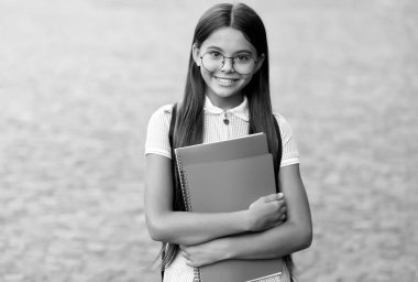 Gözlüklü mutlu ilkokul çocuğu gülüşü açık havada kitap tutuyor klasik filtre, okula geri dönüyor.