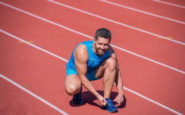 Stadyumda egzersiz yaptıktan sonra ayakkabı bağcıkları bağlayan bir adam. Spor salonu açık havada. Kaslı atletizm antrenmanı