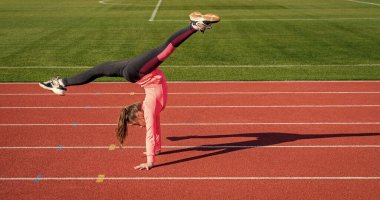 Temiz hava egzersizi. Esnek vücutlu kendine güvenen bir jimnastikçi. Jimnastik. Genç kız stadyumda numara yapıyor. Spor giyim bölümünde bir çocuk. Çocuk yarış pistinde darbe egzersizi yapıyor. sağlıklı çocukluk. İçerideki enerji