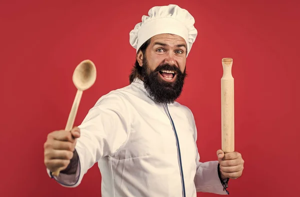 Hipster chef-kok in hoed met baard en snor op rode achtergrond gebruik maken van houten keukengerei, koken — Stockfoto