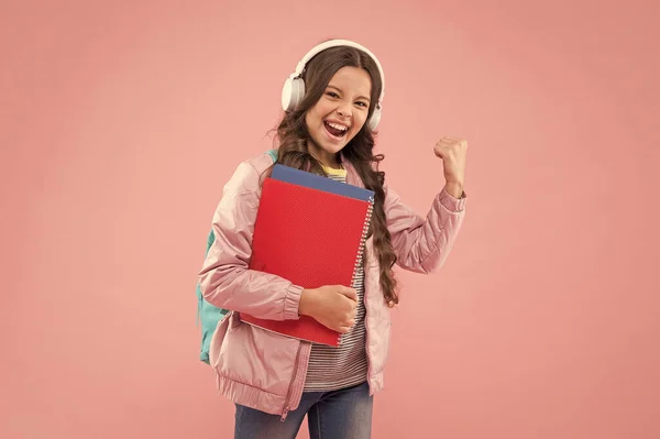 Gelukkig kind in hoofdtelefoon houden school muziek boeken maken energetische arm gebaar roze achtergrond, audio power — Stockfoto