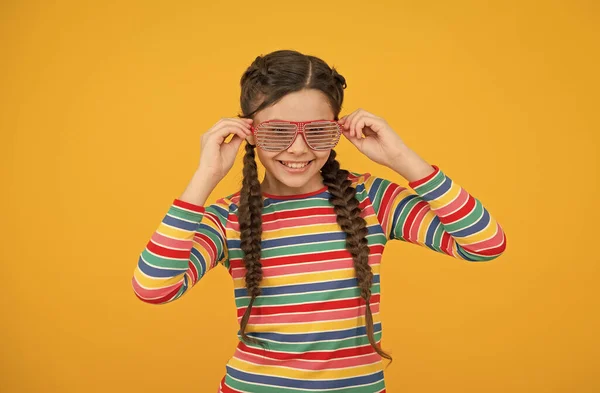 Feliz adolescente chica con trenzado pelo desgaste casual estilo arco iris color y glamour partido gafas sobre fondo amarillo, moda —  Fotos de Stock