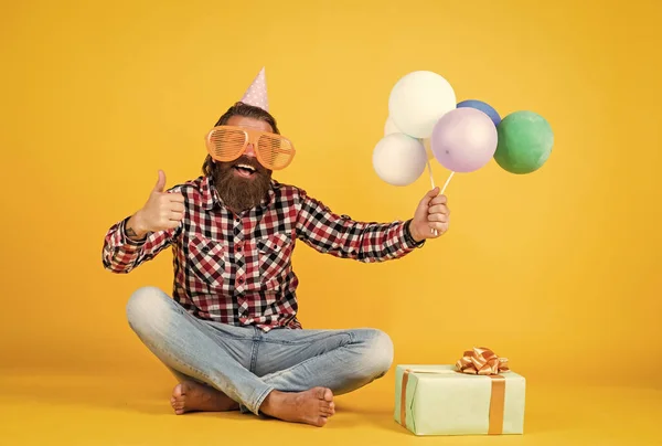 Högtidsfirande. Den skäggiga mogna mannen firar födelsedagsfest. Glada man i dag hatt hålla semester ballonger. gåvor och presenterar konceptet. Ha en trevlig semester. Dags för fest. Grattis på födelsedagen. — Stockfoto