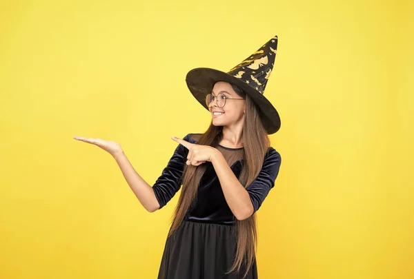 Happy witch teenage girl poiting finger on copy space wear hat costume of wizard and glasses on halloween party, happy halloween party — Stock Photo, Image