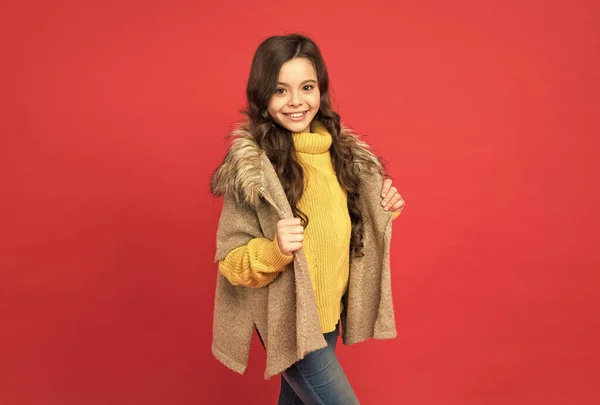 Mosolygós gyermek hosszú göndör haj viselnek meleg kötött pulóver és szőrme mellény piros háttér, divat és szépség — Stock Fotó