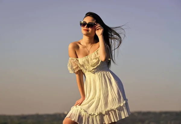 浮気をしてる。空を背景にブルネットの髪のセクシーな女の子。完璧な日没や日の出。可愛い女はサングラスをかける。女性の夏のファッション。白いドレスの屋外で官能的な美しさ。春の気分 — ストック写真