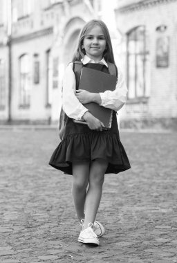 Okul üniformalı küçük bir çocuk kitap ve sırt çantası taşıyor, bilgi günü.