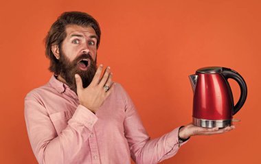 Vay canına. Bıyıklı ve sakallı vahşi bir adam. Elektrikli ev aleti. Sakallı adam kırmızı elektrikli su ısıtıcısı kullanıyor. Erkek ev idaresi konsepti. Sıcak suya ihtiyacım var. Adam çay ya da kahve içecek.