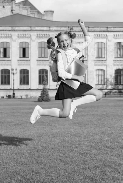 Energisk barn i formell uniform med läroböcker ryggsäck hoppa i skolgården glad firande, tillbaka till skolan — Stockfoto