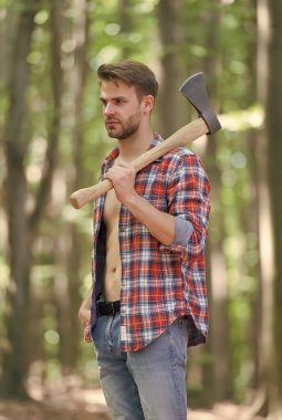 Açık ekose gömlekli, kaslı, seksi bir adam. Kot pantolonlu. Büyük bir baltası var.