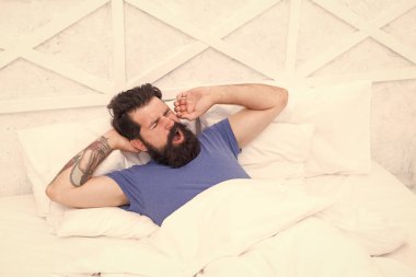 Sabah baş ağrısı olan esnemiş bir adam yatakta battaniyenin altında, erkek sağlığı