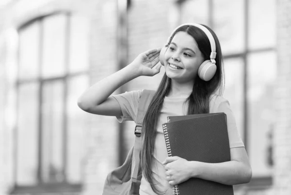 Σύγχρονο κορίτσι παιδί με ακουστικά πίσω στο σχολείο κρατήστε το βιβλίο, ήχου έννοια μάθημα — Φωτογραφία Αρχείου