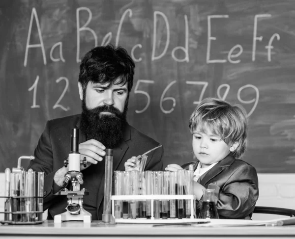 La educación es el desarrollo. Un niño pequeño con un profesor. Sabiduría. De vuelta a la escuela. sala de entrenamiento con pizarra. Frasco en mano científica con tubos de ensayo. hijo y padre en la escuela — Foto de Stock