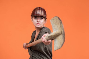 Koruyucu miğfer takan kadın işçi turuncu arka planda kürek tutuyor, endüstri