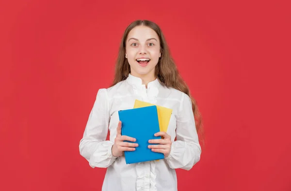 Förvånad barn i vit skjorta redo att studera göra läxor med bok om röd bakgrund, tillbaka till skolan — Stockfoto