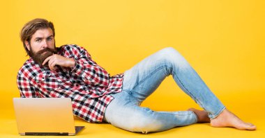 Kaba sakallı, kareli gömlek giyen, sakallı ve bıyıklı bir adam laptopta, işte çalışıyor.