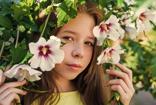 幸せな子供時代。屋外の木の開花時に明るい子供。休暇の時間だ。夏のファッションと美しさ。ハイビスカスの茂みの花を持つ美しい10代の女の子。子供の春ファッションスタイル — ストック写真