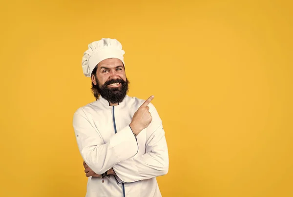 Chef masculino em chapéu com barba e bigode em fundo amarelo, apontando o dedo, espaço cópia — Fotografia de Stock