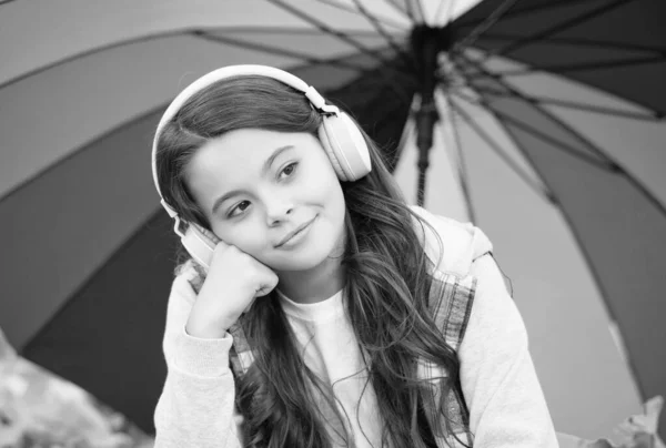 Criança feliz usar fones de ouvido sob guarda-chuva colorido. Menina ouvir música. criança relaxar na floresta de outono. folhas de outono no parque. de volta à escola. educação online. tempo chuvoso sazonal — Fotografia de Stock