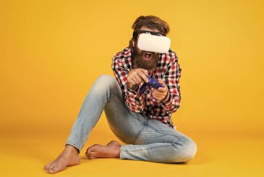 Yeni gerçekliğin tadını çıkarıyorum. Dijital gelecek ve yenilik. Sanal gerçeklik gözlüğü takan acımasız bir adam. Oyun konsolu. Adam kablosuz internet gözlüğü takıyor. VR kulaklıklı adam. Sakallı hippi modern teknoloji kullanır.