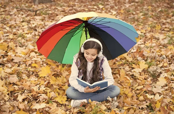 回学校去网上教育。季节性天气。快乐的孩子在五彩缤纷的雨伞下戴耳机。女孩听音乐，看书。孩子们在秋天的森林里休息。公园里的落叶 — 图库照片