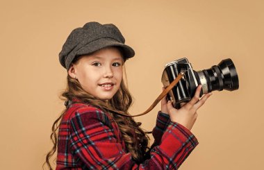 Başlıklı ve kareli ceketli neşeli çocuk klasik kamera kullanıyor, retro fotoğraf çekiyor.