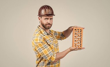 İnşaat kasklı yakışıklı teknisyen ve inşaat alanında tuğla ve mimariyle kareli gömlek.