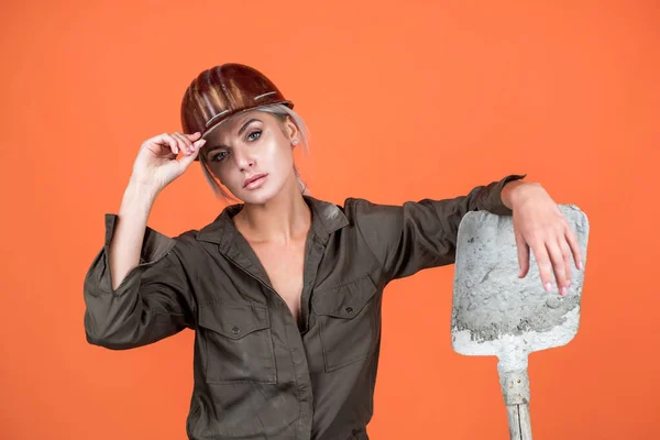 Nő dolgozó védő sisak és boilersuit tartsa lapát narancssárga háttér, munka — Stock Fotó