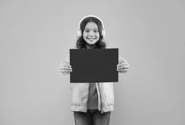 Niño alegre usando auriculares y mostrando papel vacío para espacio de copia, anuncio — Foto de Stock