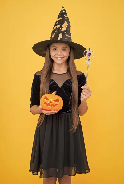 Spreuk. Een kind met een heksenhoed en pompoen. Kind creëert wonderen met toverstaf. Carnaval gekostumeerd feest. Snoep of ik schiet. Vier de feestdagen. Lantaarn. Halloween heksenmeisje. gelukkige jeugd — Stockfoto