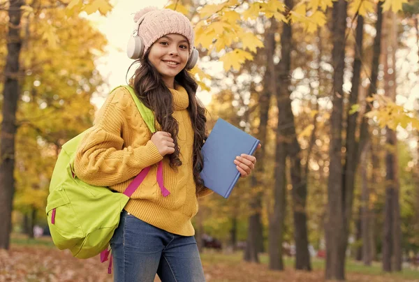 Menina com livro e mochila ouvir música em fones de ouvido, escola — Fotografia de Stock